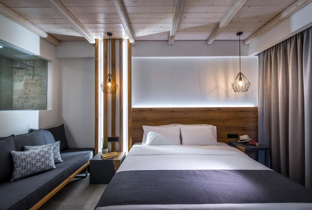 A modern hotel room with a large bed, a sofa, and a wooden headboard.