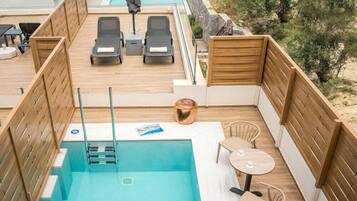 A rooftop pool area with lounge chairs, a small table, and a wooden deck.