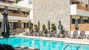 A pool area with lounge chairs and umbrellas, a stone wall, and a modern building facade.