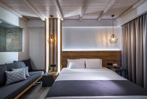 Quarto de hotel moderno com uma cama grande, um sofá, cabeceira de madeira e duas luminárias pendentes.