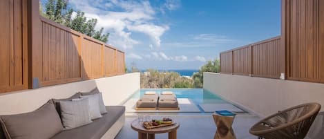 A modern outdoor lounge area with a pool, wooden furniture, and a view of the sea.