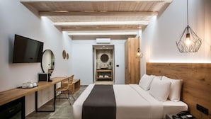 A modern hotel room with a wooden ceiling, a bed with white bedding, a desk with a computer, a TV mounted on the wall, and a unique geometric light fixture.