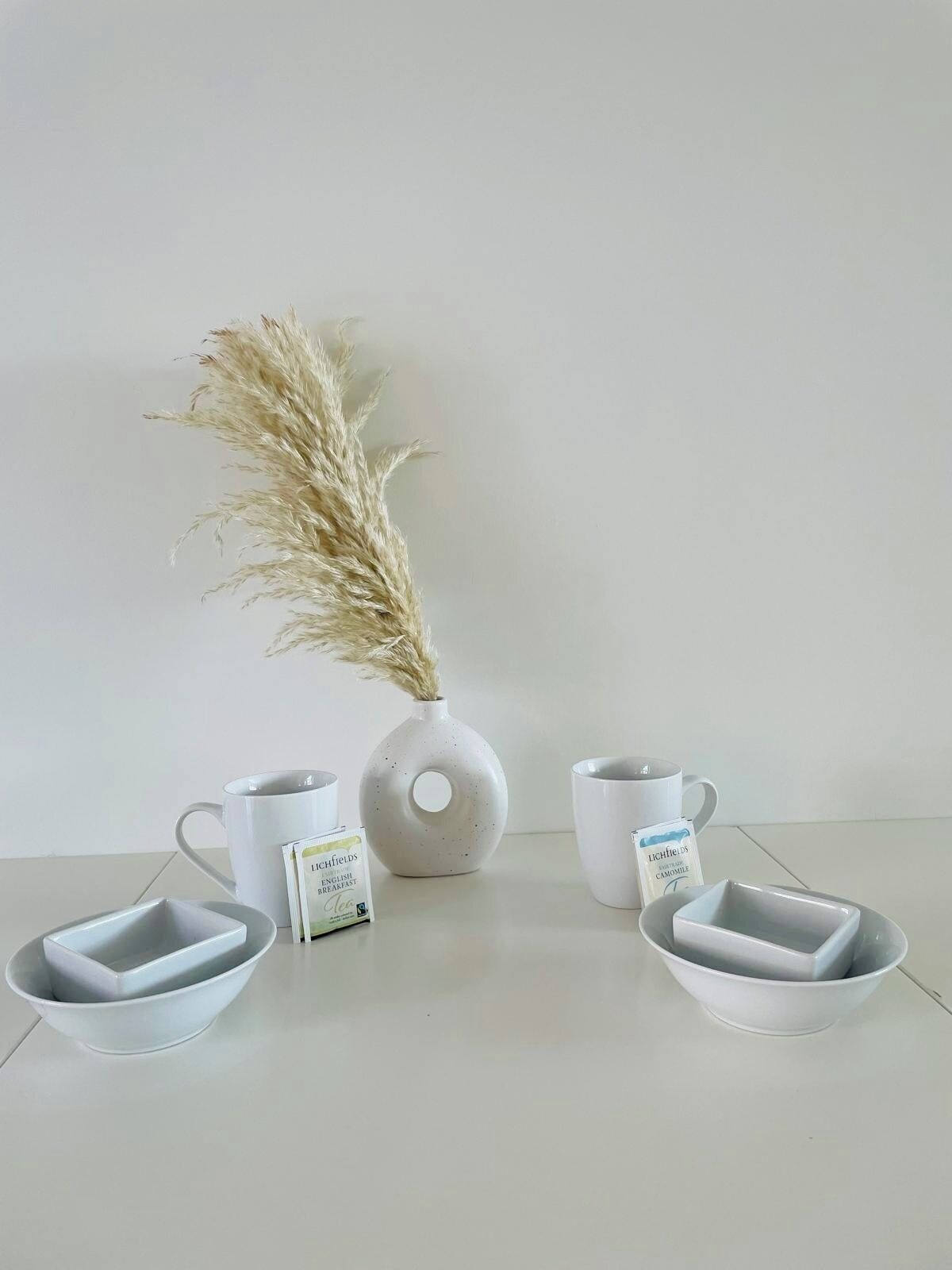 A minimalist table setting with a vase, two mugs, and two bowls.