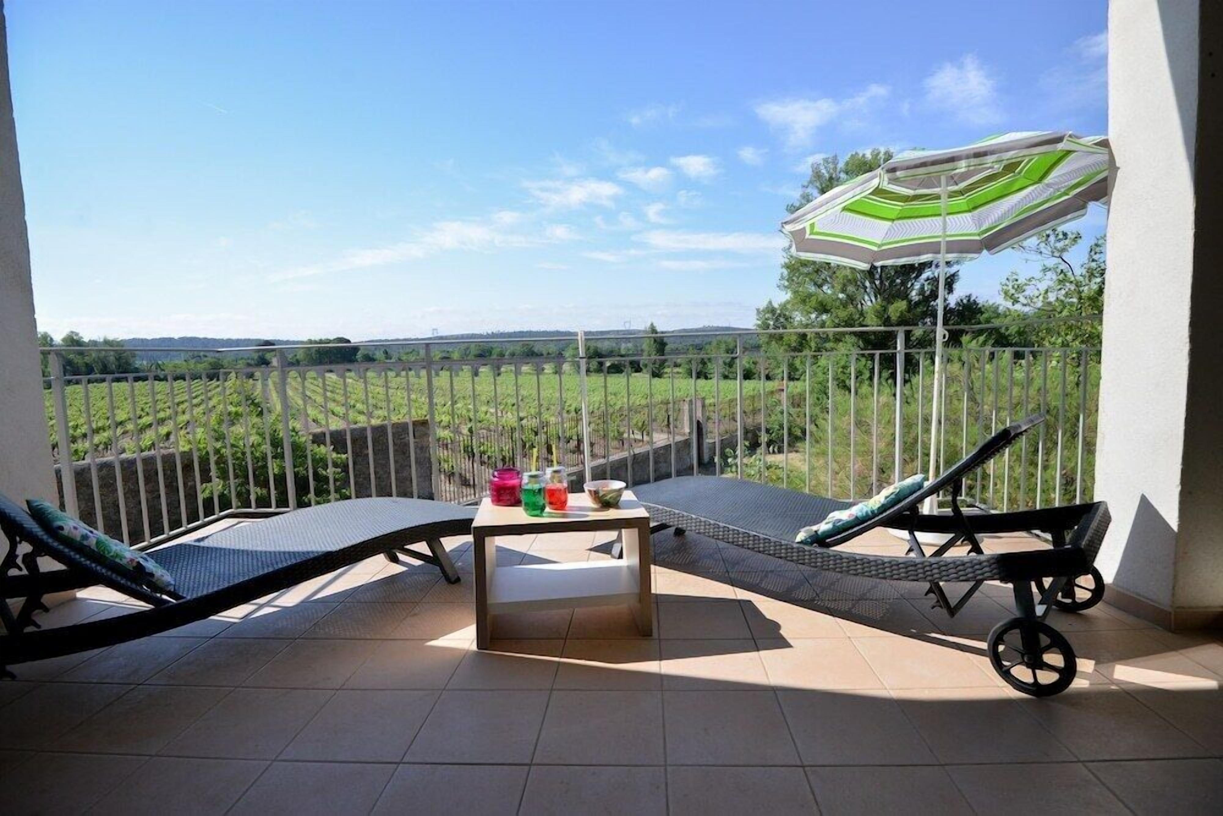 Ein Balkon mit zwei Loungestühlen, einem kleinen Tisch und einem Sonnenschirm.