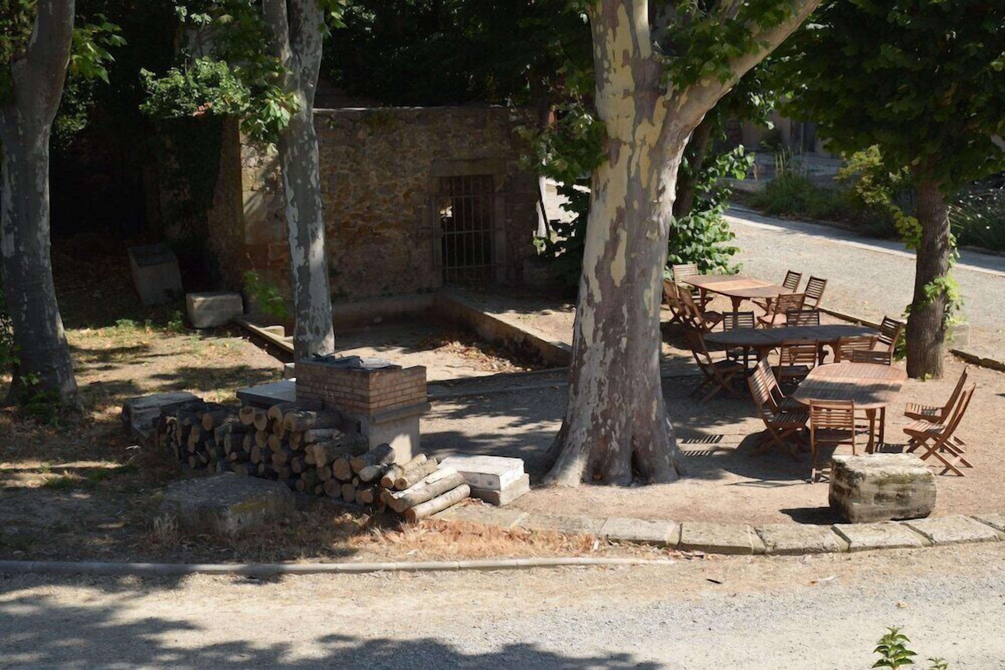 Un espacio al aire libre con muro de piedra, mobiliario de madera y árboles.