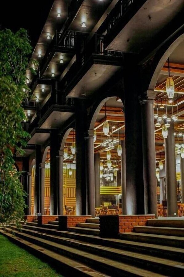 Un edificio con varios arcos y columnas, zonas de estar al aire libre y lámparas colgantes.