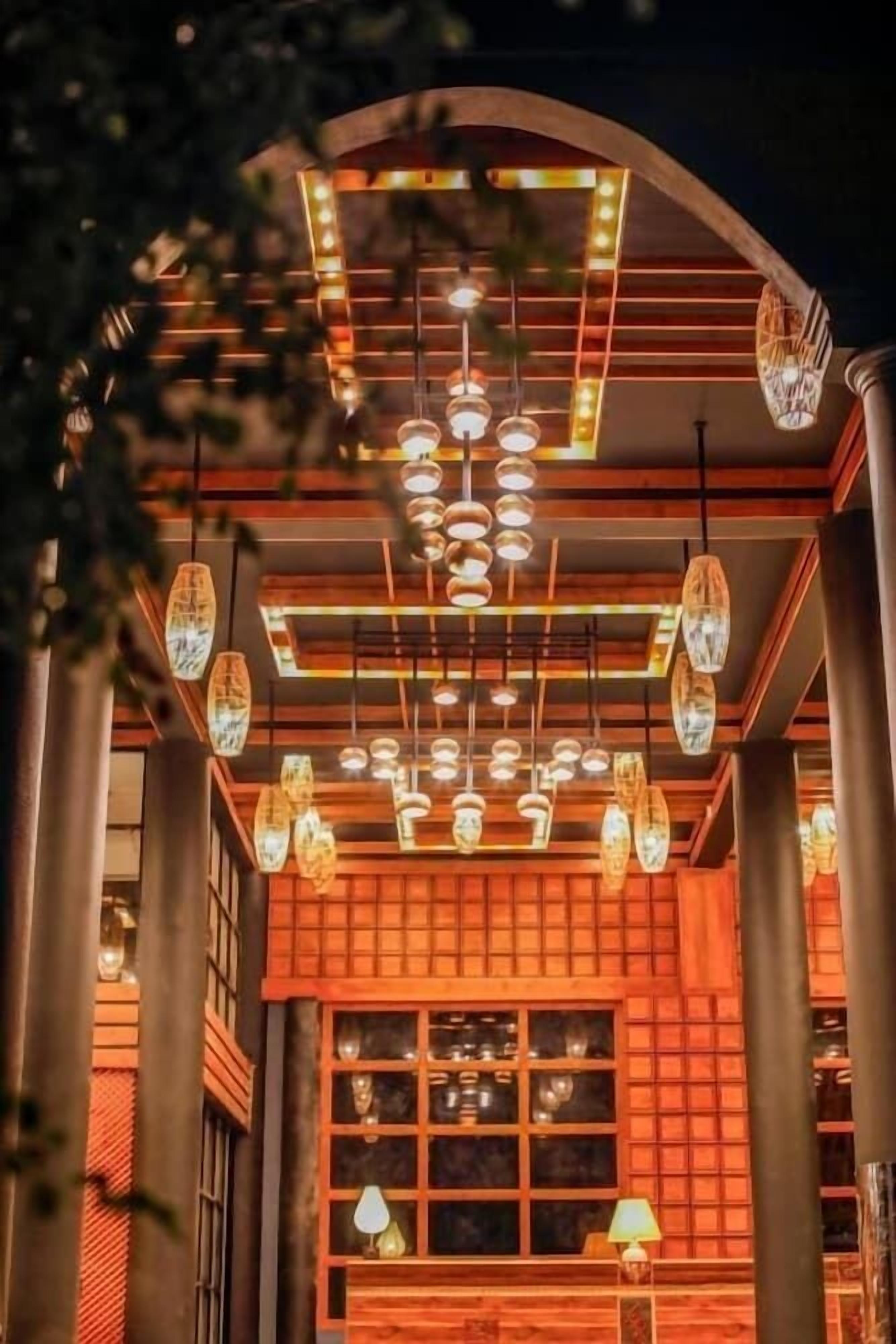 A warmly lit interior with a traditional wooden facade, multiple hanging light fixtures, and a window with a view.