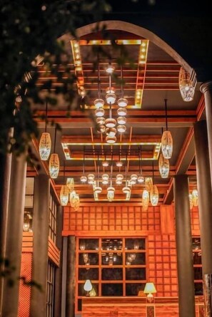 Interior cálidamente iluminado, con fachada de madera tradicional, múltiples lámparas colgantes y una ventana que ofrece vistas.