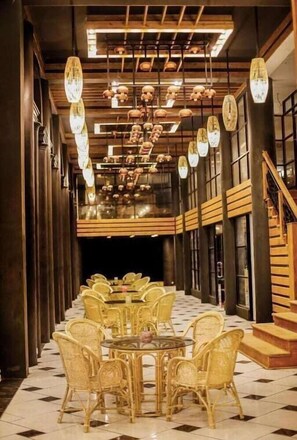 A long corridor with a central dining area featuring round tables and wicker chairs, flanked by wooden walls and a staircase. - Covanro Sigiriya (Avudangawa)