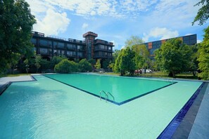 Una piscina con superficie de agua azul cristalina, rodeada de árboles y un edificio de estilo arquitectónico moderno.