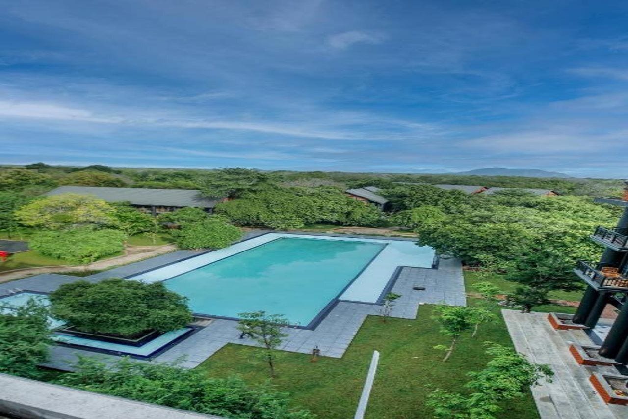 Une grande piscine rectangulaire entourée de verdure et un bâtiment doté d’un toit plat.