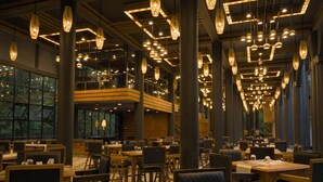 A restaurant with multiple dining tables and chairs, large windows, and hanging pendant lights. - Covanro Sigiriya (Avudangawa)