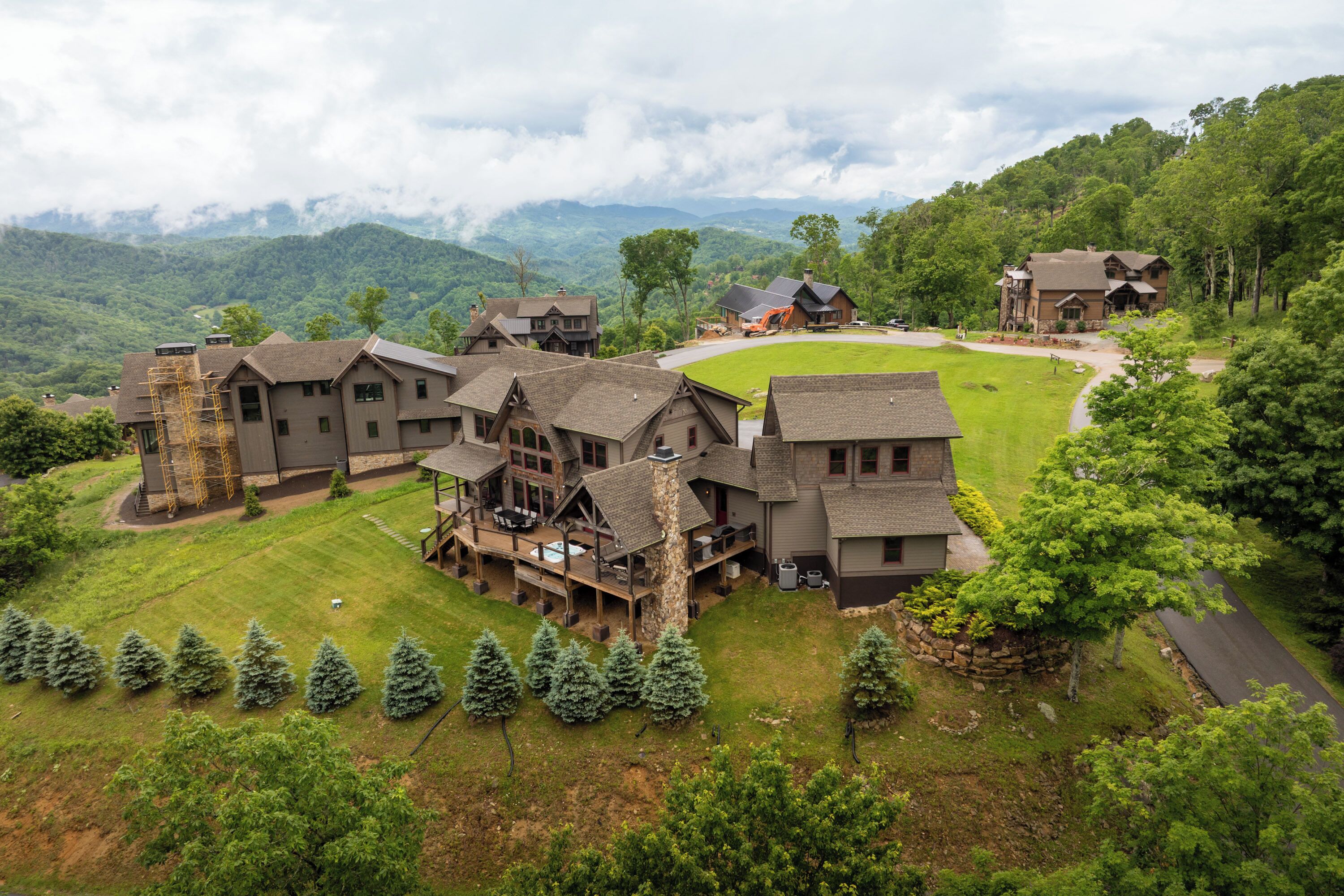 A large, multi-story building with a spacious deck and outdoor hot tub, surrounded by lush greenery and mountains in the background.