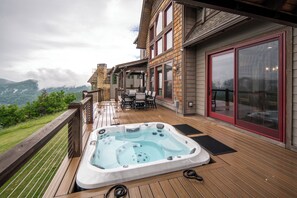 A wooden deck with a hot tub, outdoor furniture, and a view of a mountainous landscape. - Buffalo Whiskey Soak Above the Clouds at a Luxe 5BR Eagle's Nest Lodge (Banner Elk)