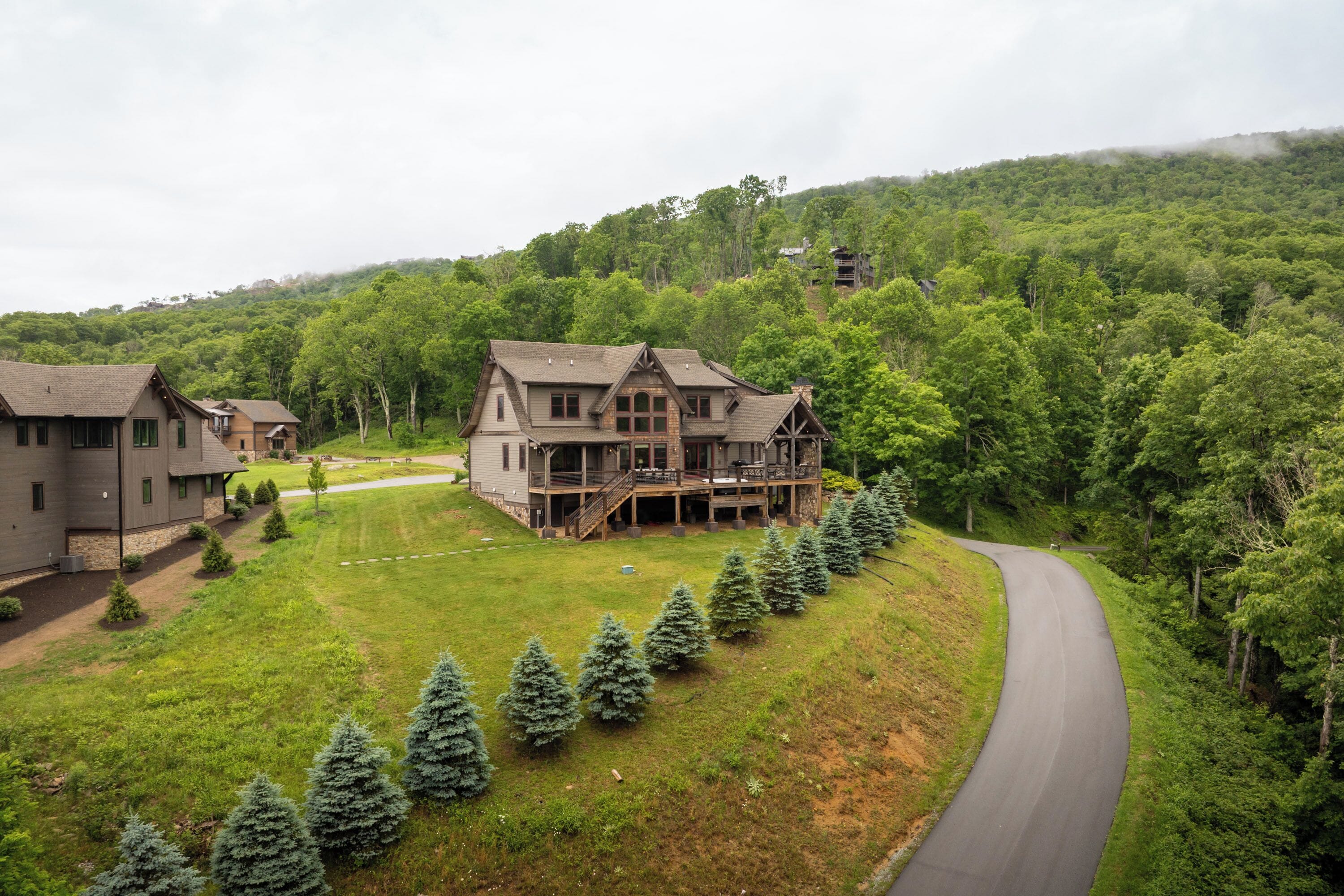 A large, two-story house with a porch and a deck, surrounded by a well-maintained lawn and a row of evergreen trees.