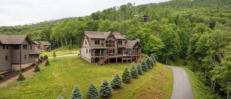 A large, two-story house with a porch and a deck, surrounded by a well-maintained lawn and a row of evergreen trees.