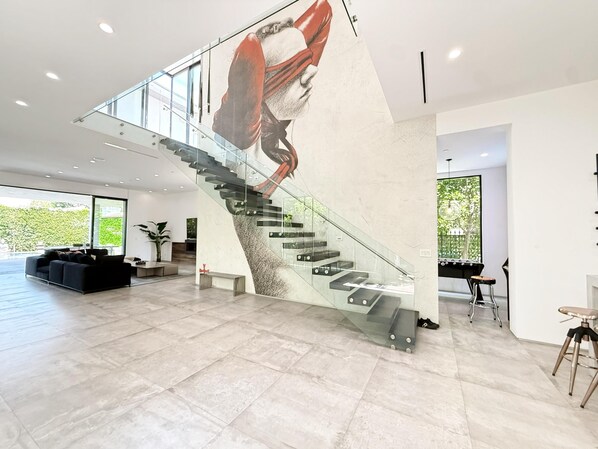 A modern interior with a glass staircase, a black sofa, and a dining area with a table and chairs. - Modern Museum 5-bedroom infinity pool (Los Angeles)