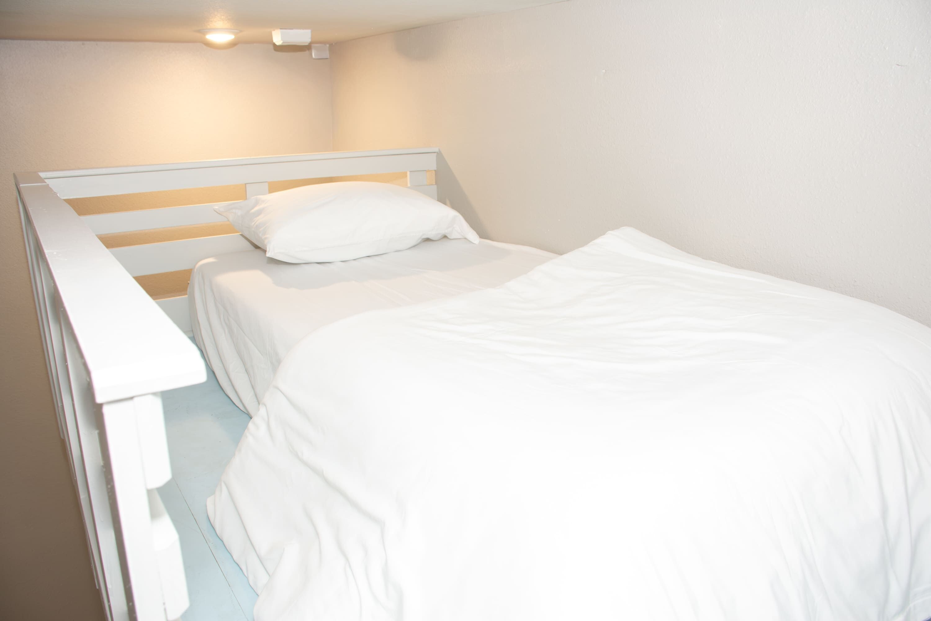 A single white bed with a wooden headboard in a room with white walls and a light-colored floor.