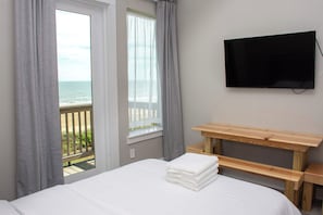 Ein Hotelzimmer mit Bett, einem an der Wand befestigten Fernseher und Meerblick durch das Fenster.