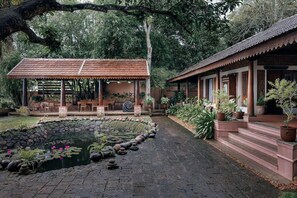 A traditional building with a tiled roof, a pond with lotus flowers, and a garden with potted plants. - Blusalzz Escapade - Muhamma, Alleppey - Kerala by Zuzu (Cherthala)