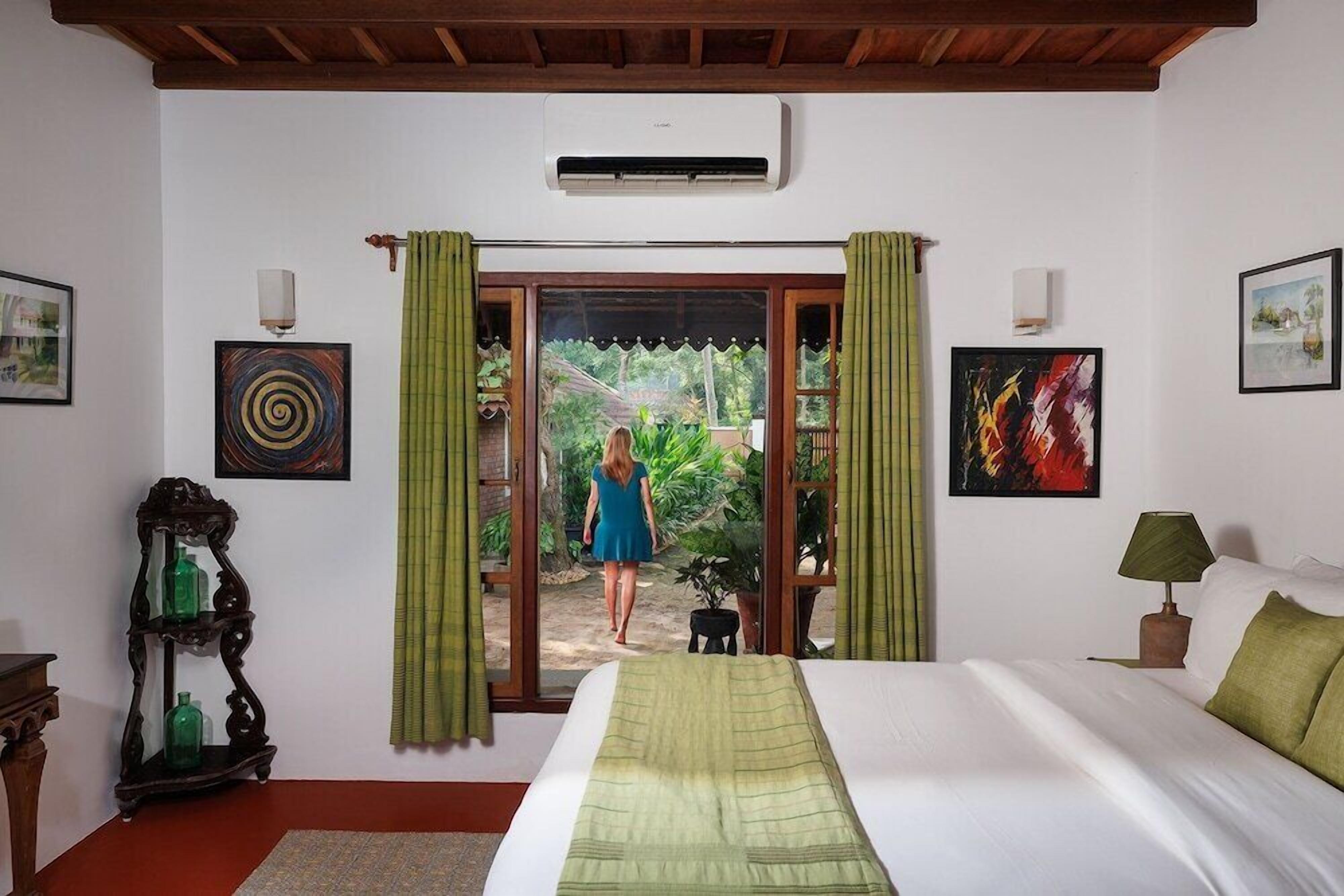 A bedroom with a bed, a window with curtains, a wall-mounted air conditioner, and artwork.