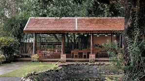 Área de estar coberta ao ar livre, com lagoa de pedra e vegetação ao redor.
