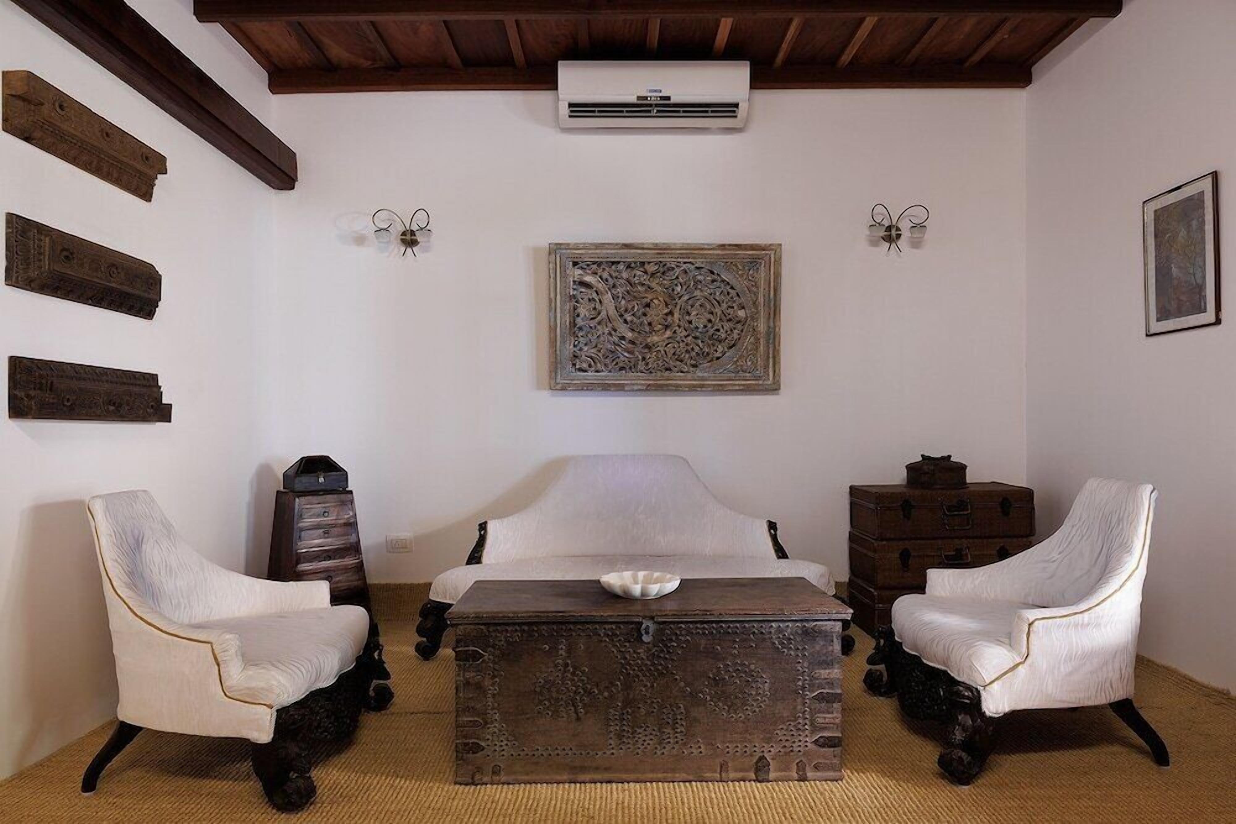 Quarto com cama, duas poltronas, cômoda, ar-condicionado fixado na parede e uma obra de arte emoldurada.