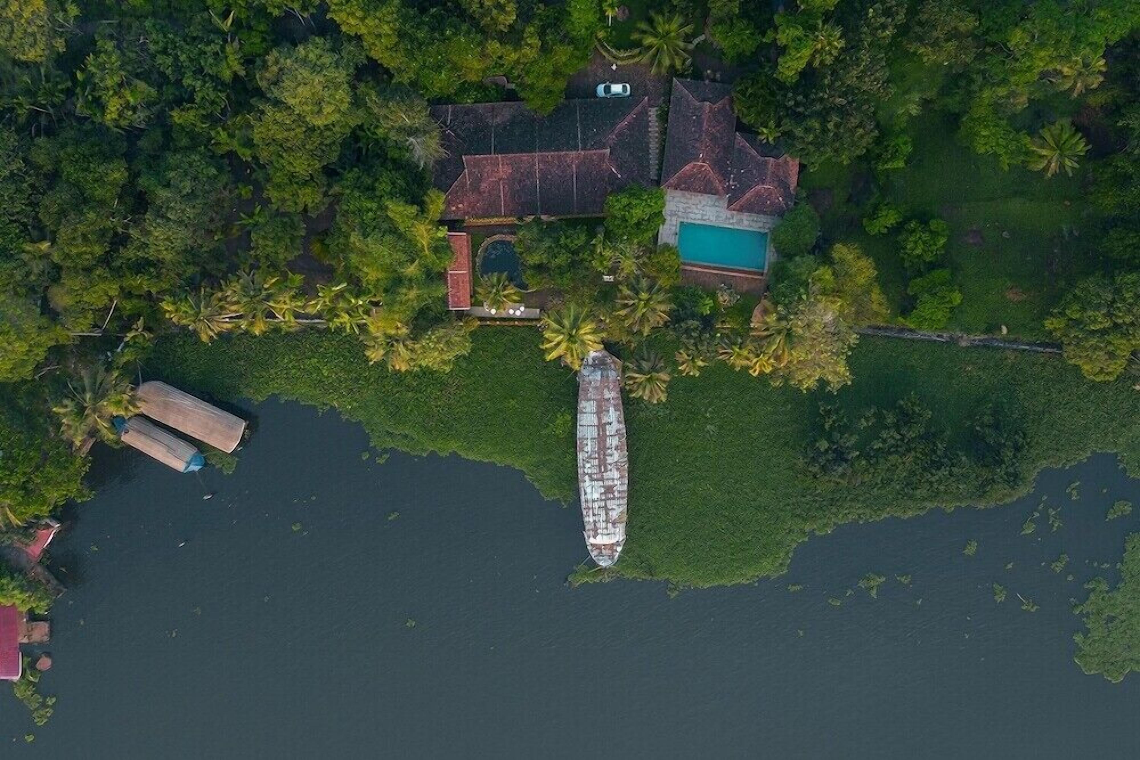 Vista aérea de uma propriedade com piscina, um cais para barcos e vegetação exuberante.