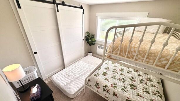 A bedroom with a single bed, a small bedside table, a nightstand, a window with blinds, and a door with a black handle. - Teton View Farm Stay—Newly remodeled whole home! 3 spacious bedrooms, 2 baths (Unknown)