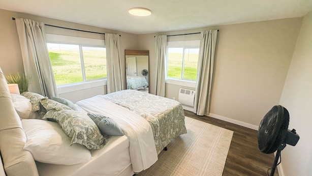 A bedroom with a bed, a standing fan, and a window with curtains. - Teton View Farm Stay—Newly remodeled whole home! 3 spacious bedrooms, 2 baths (Unknown)
