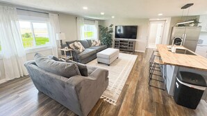 A modern living room with a grey sofa, a flat-screen TV, and a wooden dining table. - Teton View Farm Stay—Newly remodeled whole home! 3 spacious bedrooms, 2 baths (Unknown)