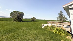 A grassy field with a wooden deck and a building with a sloped roof. - Teton View Farm Stay—Newly remodeled whole home! 3 spacious bedrooms, 2 baths (Unknown)