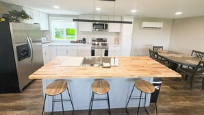 A modern kitchen with a central island, bar stools, stainless steel appliances, and a dining area with a table and chairs. - Teton View Farm Stay—Newly remodeled whole home! 3 spacious bedrooms, 2 baths (Unknown)