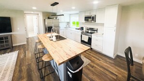 A modern kitchen with a wooden island, stainless steel appliances, and a view to the living area. - Teton View Farm Stay—Newly remodeled whole home! 3 spacious bedrooms, 2 baths (Unknown)