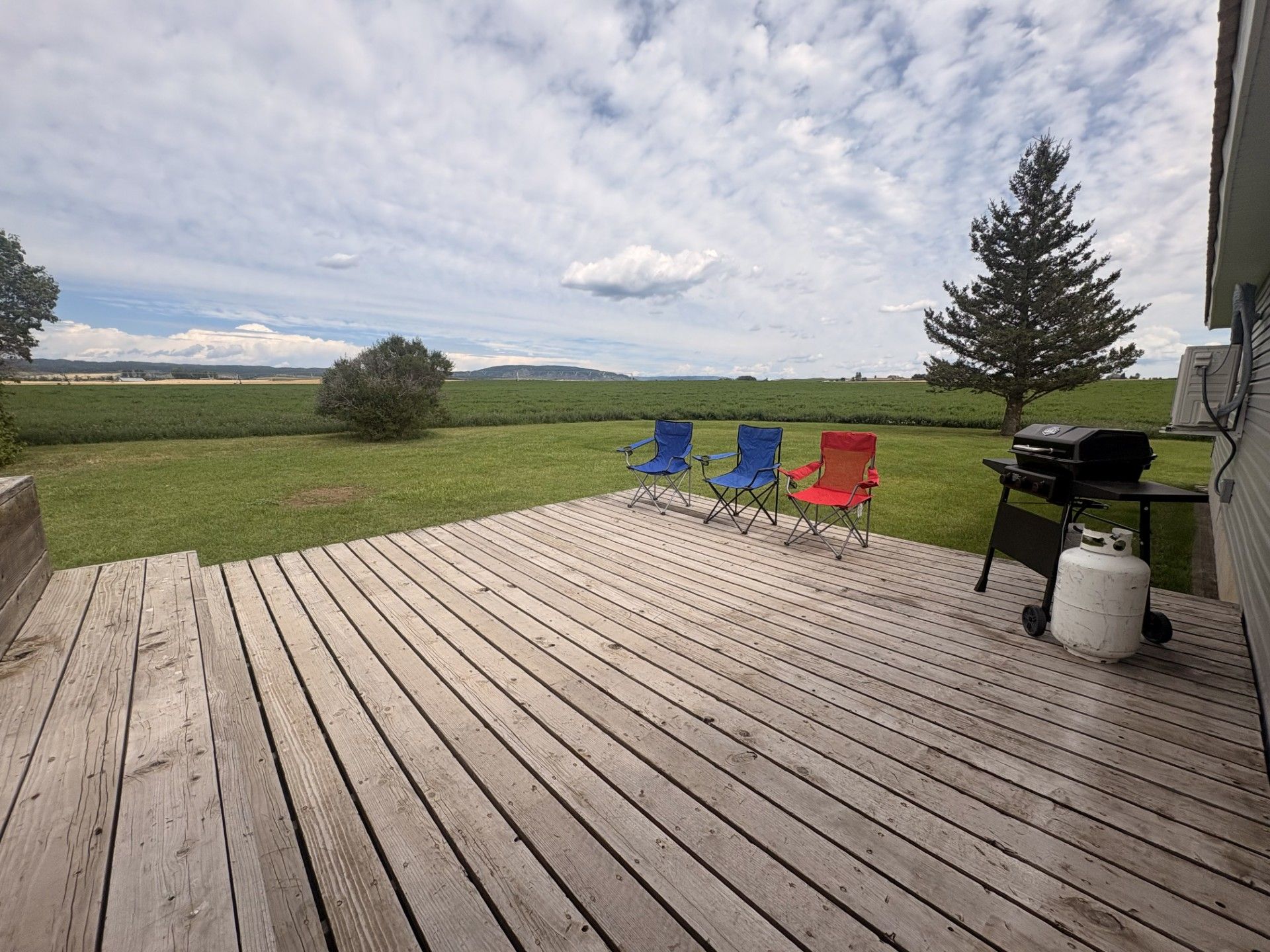 Une terrasse en bois avec deux chaises pliantes, un barbecue et une bouteille de propane.