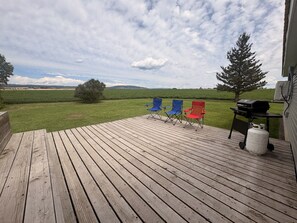 Una terraza de madera con dos sillas plegables, una parrilla y un tanque de propano.