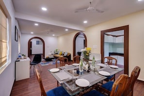 A dining area with a glass table, wooden chairs, and a ceiling fan. - De Garland, Palolem - AM Hotel Kollection (Canacona)