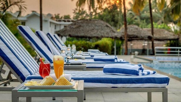 Un espace aménagé au bord de la piscine, avec des chaises longues, une table où sont servis des boissons et des collations, et des parasols en chaume.
