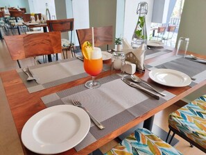 Una mesa de comedor dispuesta con un vaso de jugo de naranja, una botella de agua y un salero y pimentero.