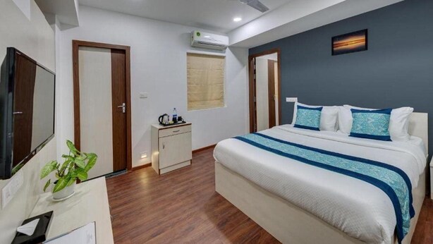 A hotel room with a bed, a desk, a television, an air conditioning unit, and a ceiling fan. - De Garland, Palolem - AM Hotel Kollection (Canacona)