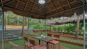 An outdoor dining area with a thatched roof, wooden tables, and chairs. - De Garland, Palolem - AM Hotel Kollection (Canacona)