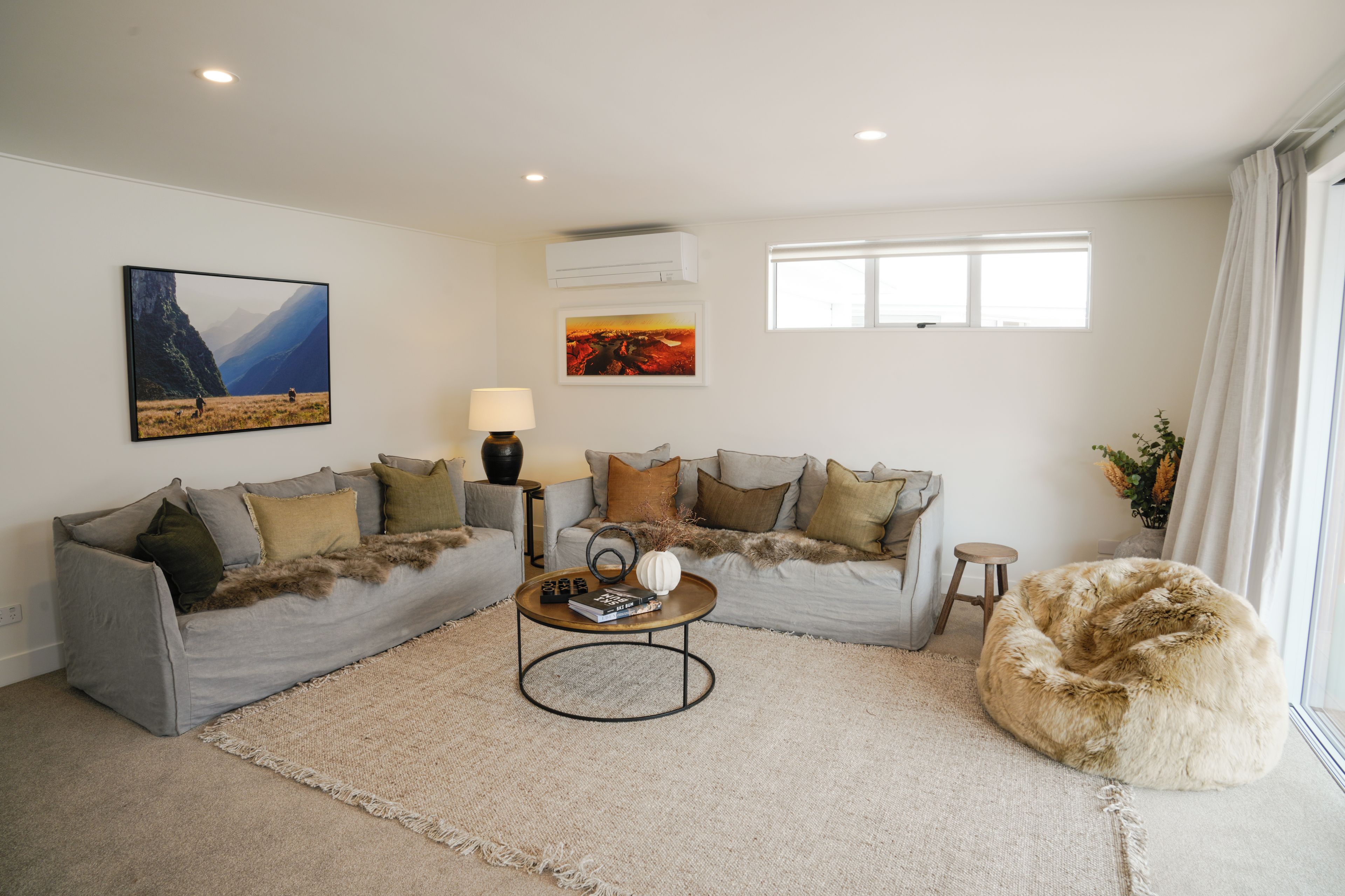 A living room with a sectional sofa, a coffee table, a shaggy pouf, and artwork on the walls.