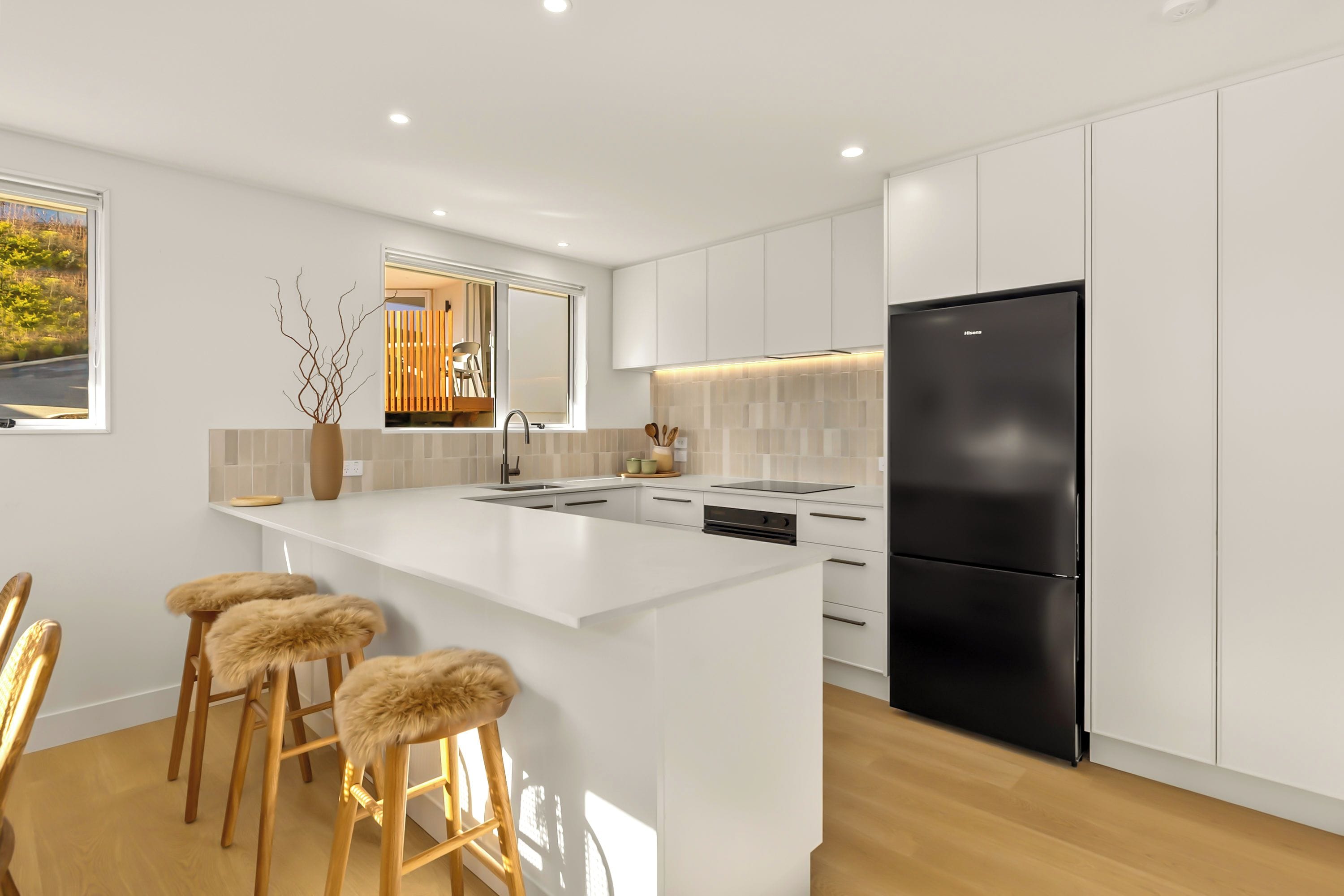 A modern kitchen with white cabinetry, a black refrigerator, and a central island with bar stools.