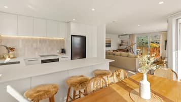 A modern kitchen with white cabinetry, a black refrigerator, and a dining area with a wooden table and rattan chairs.
