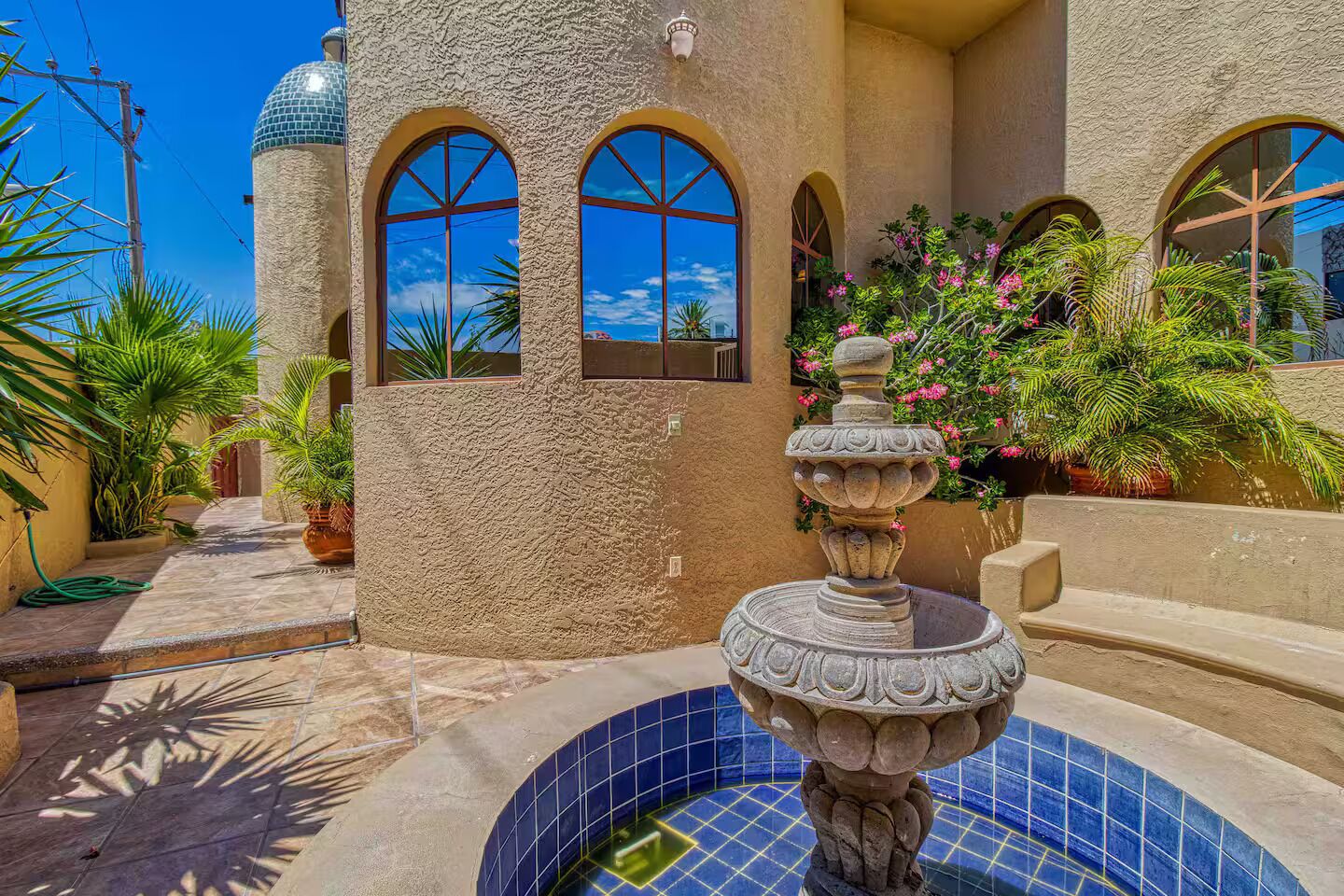 A courtyard with a fountain, arched windows, and potted plants.