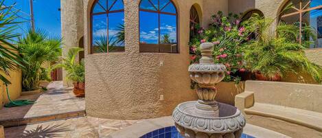 A courtyard with a fountain, arched windows, and potted plants.