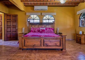 A bedroom with a wooden bed, two bedside tables, a large window with a view, and an air conditioning unit on the wall. - Ocean views, close to beach and marina boardwalk! (San Carlos Nuevo Guaymas)