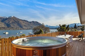 Un jacuzzi en una terraza de madera con vistas a un lago y montañas.