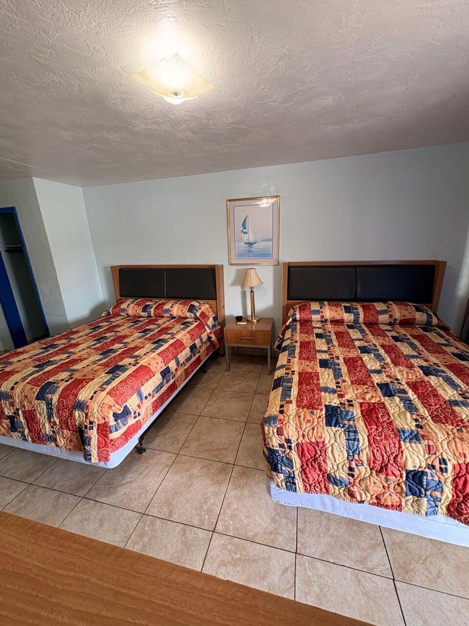 A room with two beds, a nightstand, a lamp, and a framed picture on the wall.