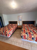 Una habitación con dos camas, una mesita de noche, una lámpara y un cuadro en la pared.